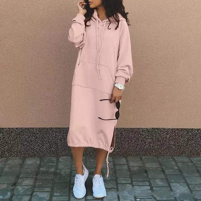 Woman wearing a loose pink hoodie dress with drawstrings, long sleeves, and white sneakers