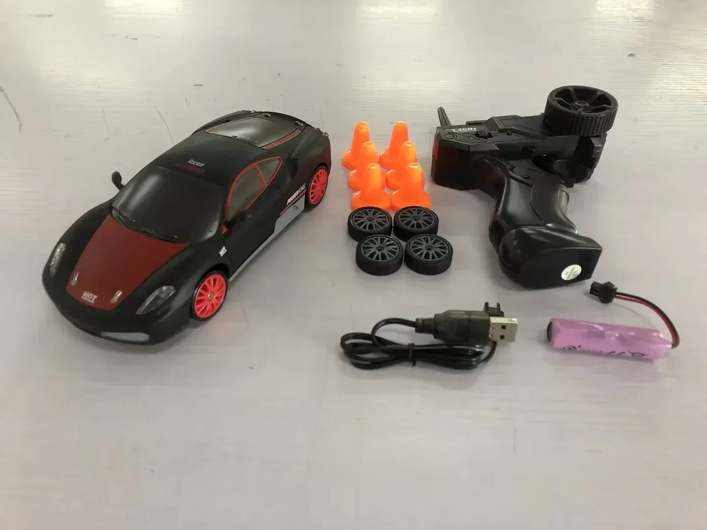 Black and red RC sports car toy set with controller, extra wheels, cones, USB cable, battery