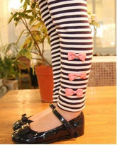 Child wearing black and white striped leggings with pink bows and black patent shoes