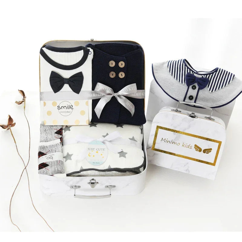 Baby gift set with navy and white clothing, knit sweater, bow tie, socks, and star-patterned blanket in a decorative box.