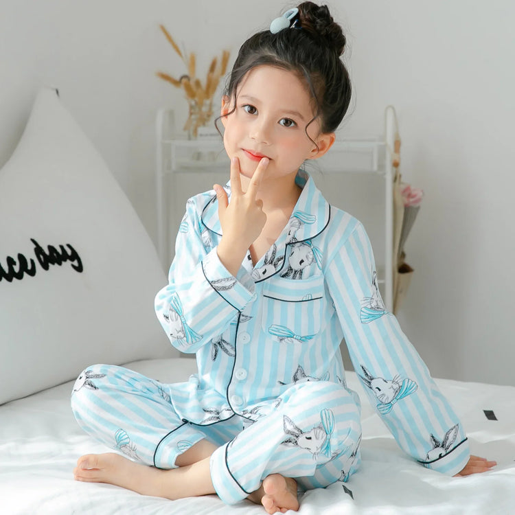 Child wearing light blue striped long-sleeve pajamas with bunny print, sitting on bed