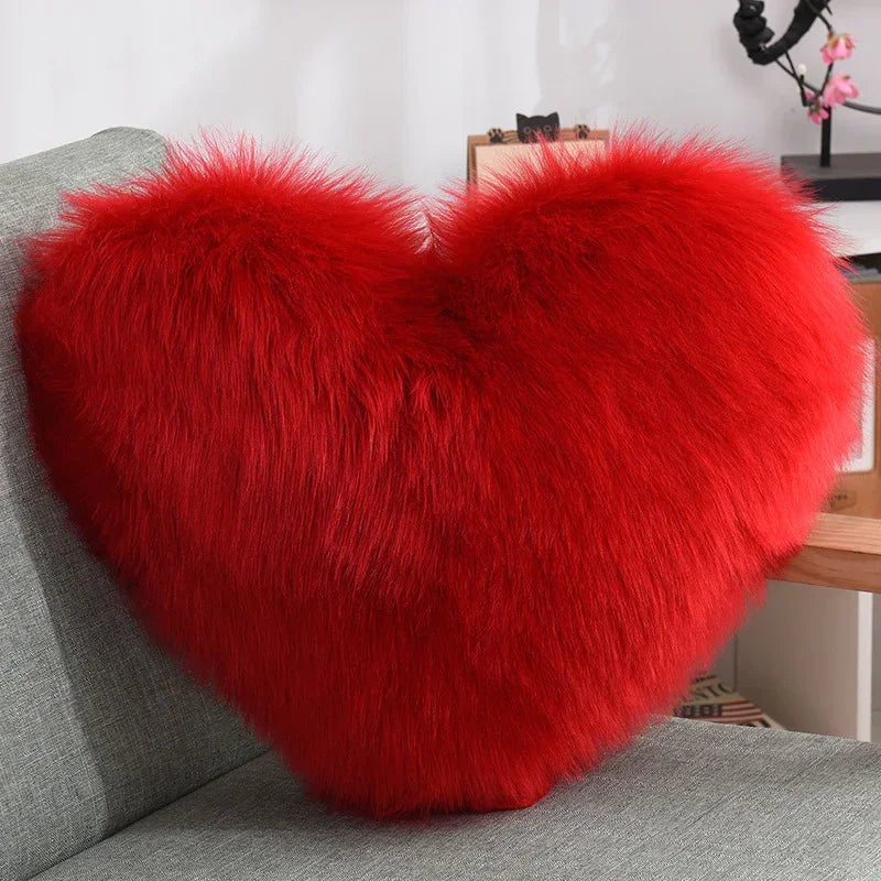 Red fluffy heart-shaped pillow with soft faux fur texture on a gray sofa