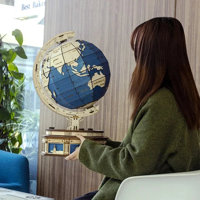 Woman in loose fit, olive green wool coat holding a blue and beige globe indoors