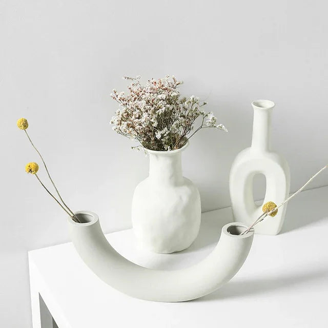 Minimalist white ceramic vases with textured finish, featuring dried flowers, on a white table