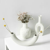 Minimalist white ceramic vases with textured finish, featuring dried flowers, on a white table