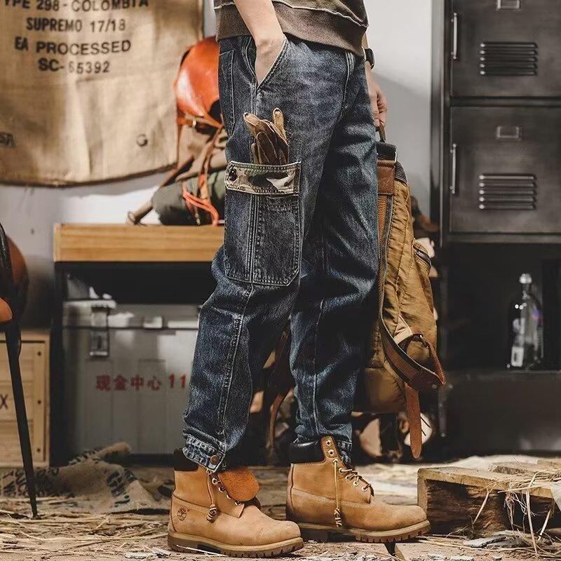 Relaxed fit dark wash denim cargo pants with camo pocket details, paired with tan work boots.