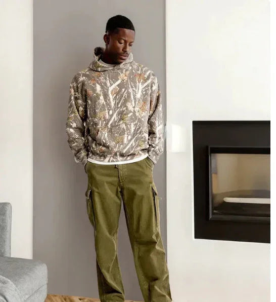 Man wearing oversized camouflage hoodie and loose olive green cargo pants indoors