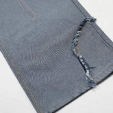 Close-up of blue denim pant leg with raw edge distressed hem, straight fit style