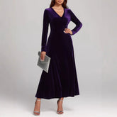 Woman wearing a long-sleeve, deep purple velvet maxi dress with a V-neck and fitted waist