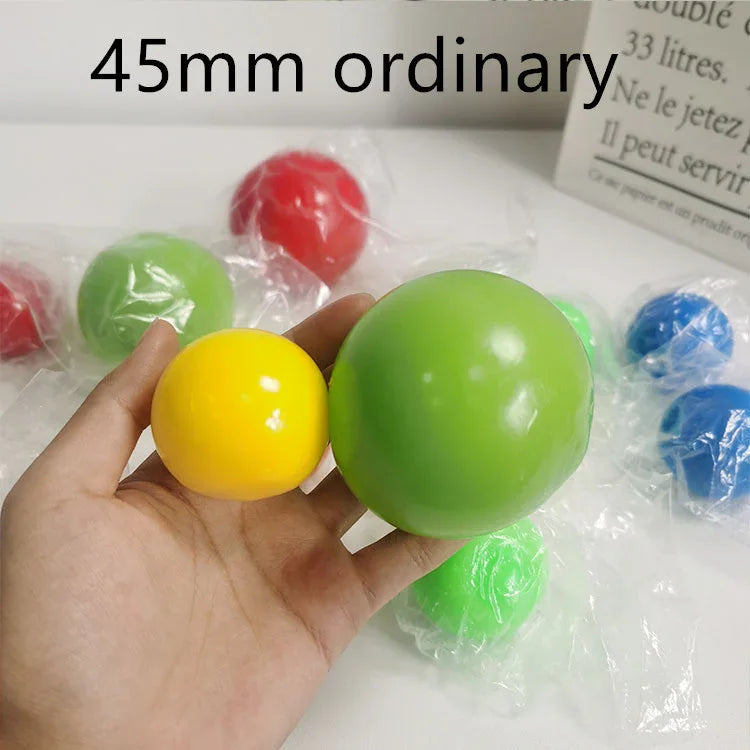 Hand holding yellow and green plastic balls, assorted colored balls in background
