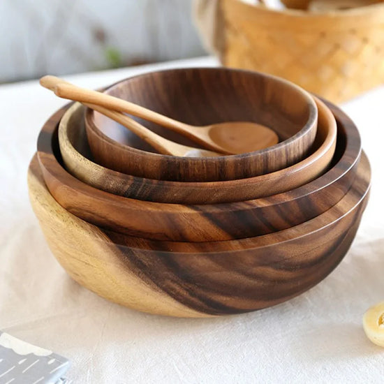 Set of wooden nesting bowls with natural grain, accompanied by wooden serving spoons, on a table.