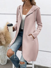 Woman wearing a light pink zip-up hooded jacket, white tank top, and ripped jeans, relaxed fit