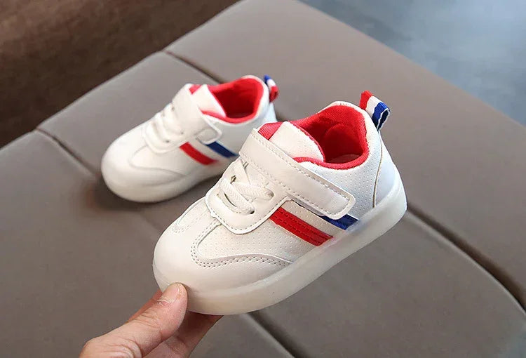 White toddler sneakers with red and blue stripes, velcro strap, and soft cushioned fit