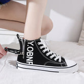 Black canvas high-top sneaker with white laces, side zipper, and bold white text, relaxed fit