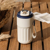 White insulated tumbler with navy blue lid and carrying strap on wooden table