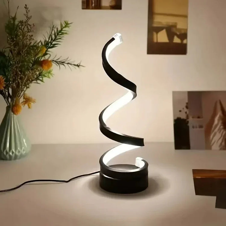 Modern spiral LED desk lamp with black and white finish on a minimalist table.