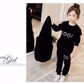 Little girl in black velvet streetwear set with white lettering, relaxed fit, white sneakers