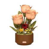Artificial peach roses in a round brown planter, detailed with green leaves and small yellow flowers.