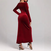 Woman wearing a long-sleeve, fitted burgundy velvet maxi dress with a back slit