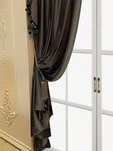 Dark gray velvet curtain with tassel and pom-pom trim, draped by a window