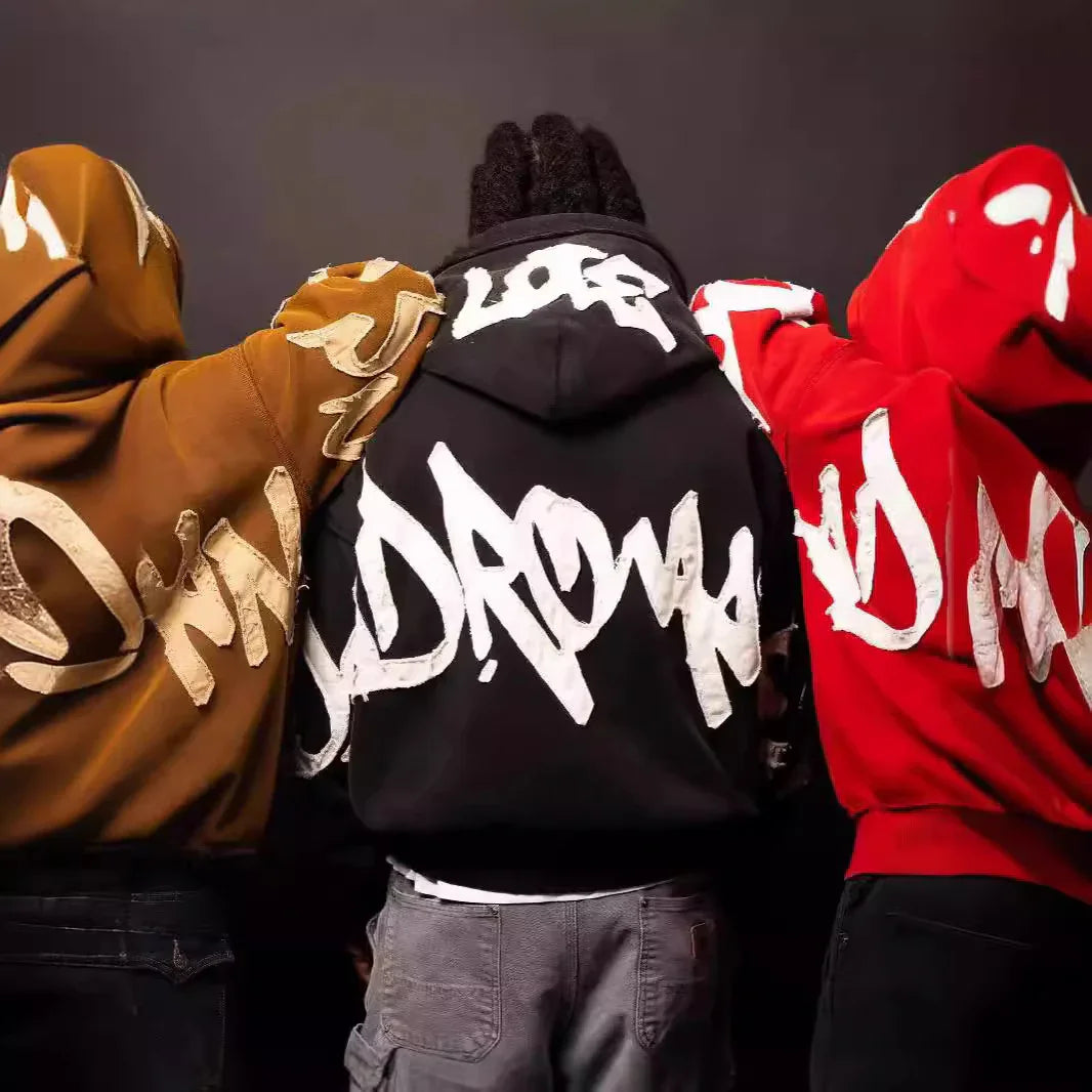 Three people in oversized streetwear hoodies with bold graffiti print, in brown, black, and red.