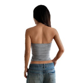 Woman wearing a fitted gray strapless top and relaxed blue denim jeans, back view