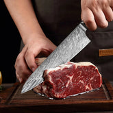 Hand slicing raw marbled beef with a patterned chef knife on a wooden cutting board
