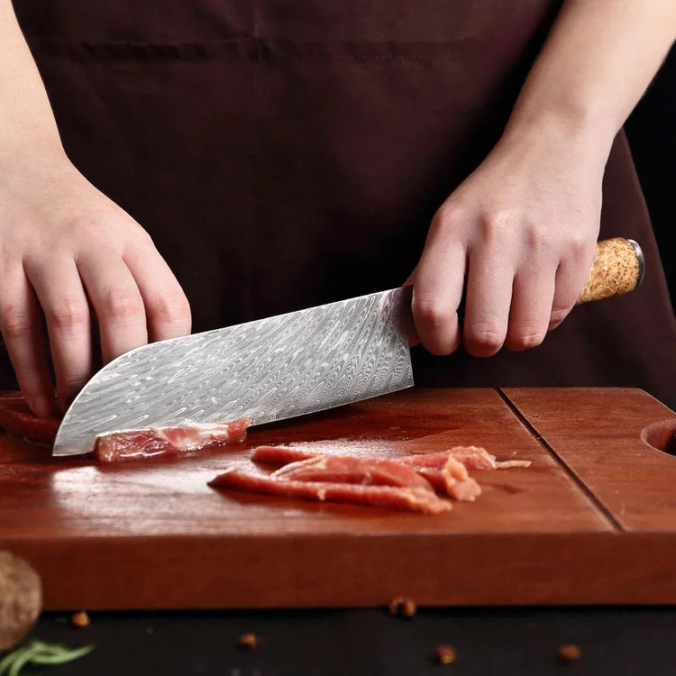 Person in a dark apron slicing raw meat on a wooden cutting board