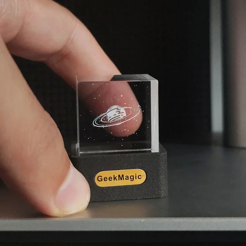 Clear acrylic cube with etched planet design and stars, held between fingers, on display base