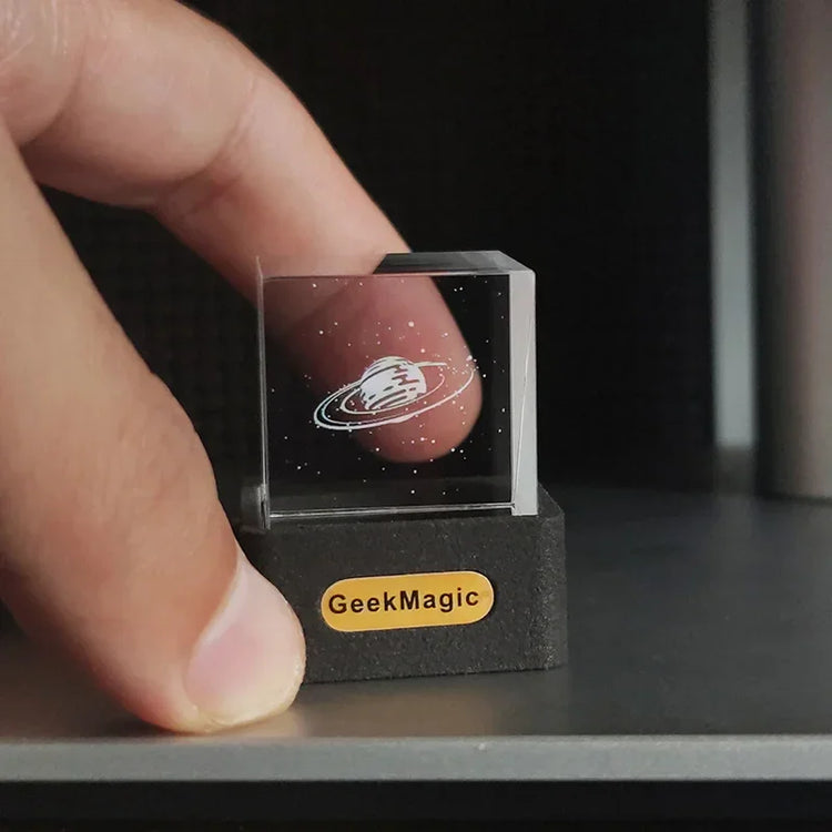 Clear acrylic cube with etched planet design and stars, held between fingers, on display base