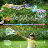 Young boy in a yellow striped short sleeve shirt outdoors, using a plastic bubble wand to blow large and small bubbles, standing on green grass with trees in the background.