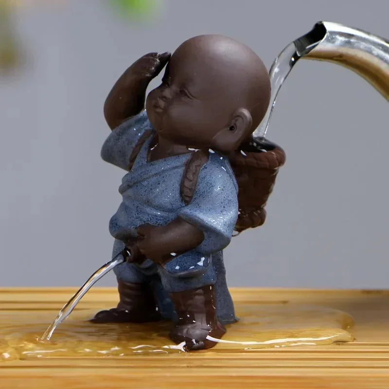 Small ceramic monk figurine in blue robe, pouring water fountain, on wooden surface