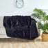 Black waterproof blanket draped over beige sofa in modern living room with wall clock and green plant.