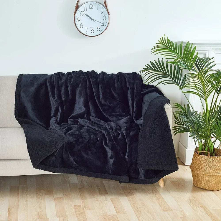 Black waterproof blanket draped over beige sofa in modern living room with wall clock and green plant.
