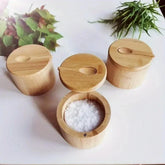 Set of round bamboo spice containers with lids, one open showing salt, on a white table