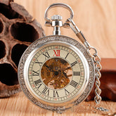 Silver vintage pocket watch with Roman numerals and exposed mechanical gears on wood surface.