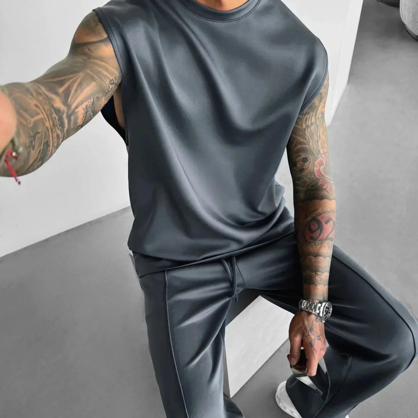 Man wearing dark gray sleeveless top and matching relaxed fit pants, modern streetwear style