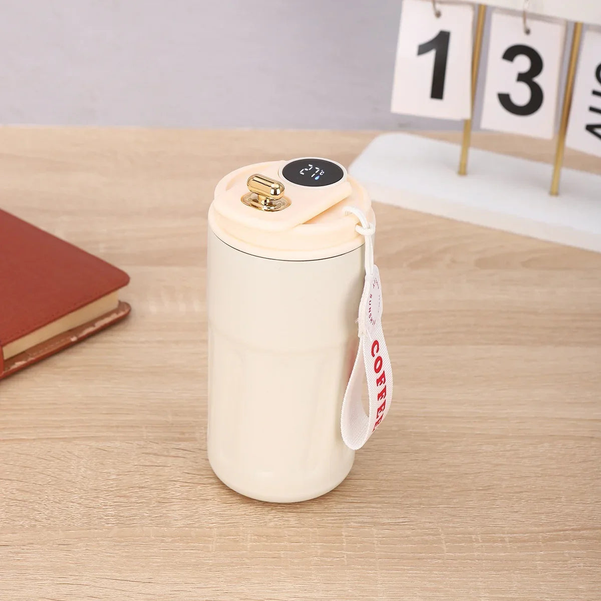 Cream insulated travel mug with digital temperature display and carrying strap on wooden desk