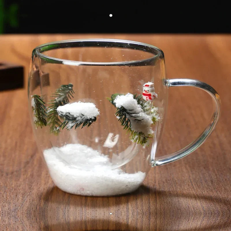 Clear glass mug with snow, pine branches, and miniature snowman on wooden table
