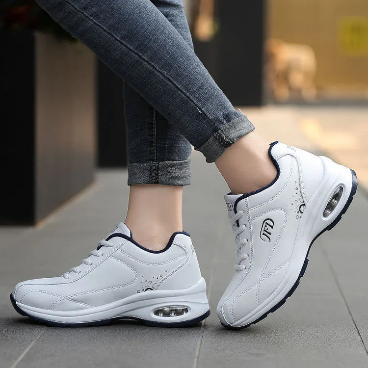 White athletic sneakers with air-cushioned sole, low-top design, worn with rolled jeans.