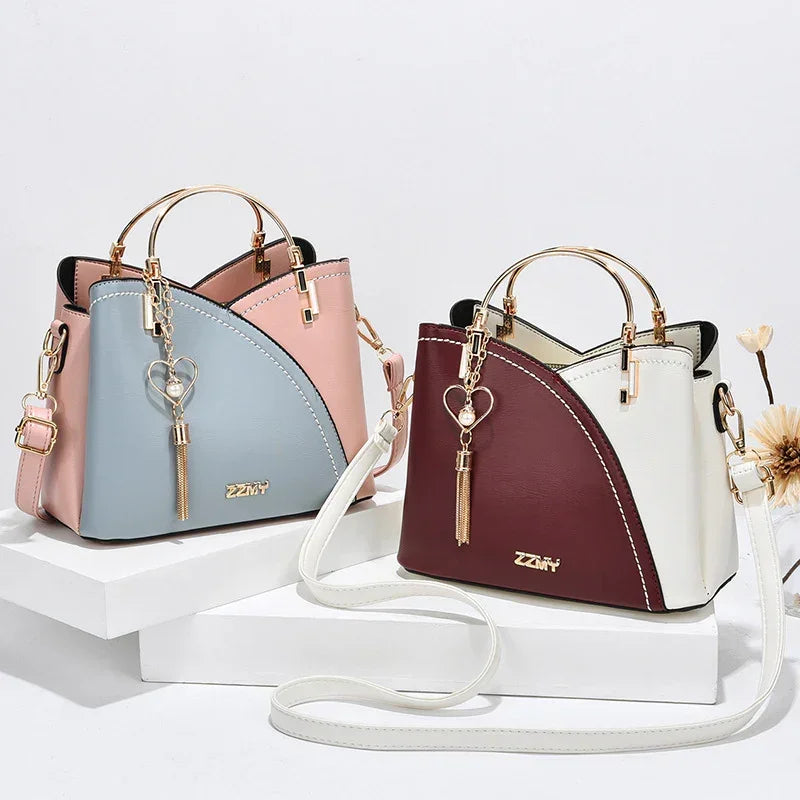 Two colorblock faux leather handbags with gold hardware, top handles, and heart keychain, one in pink and blue, one in burgundy and white.