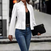 Woman wearing a fitted white blazer, black top, blue jeans, and holding a black clutch