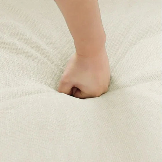 Hand pressing into soft, beige textured fabric showcasing cushion material and plush feel