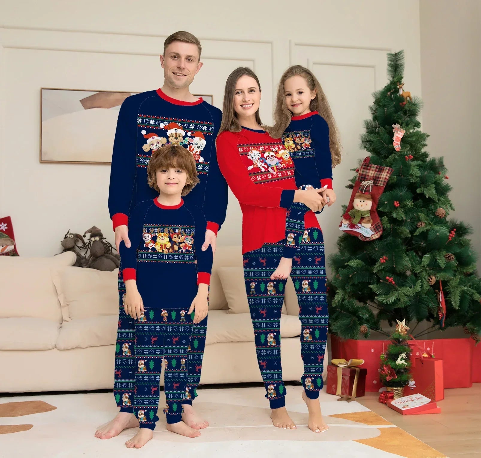 Family wearing matching festive cartoon print pajamas with long sleeves and navy blue, red accents, standing by a Christmas tree indoors.