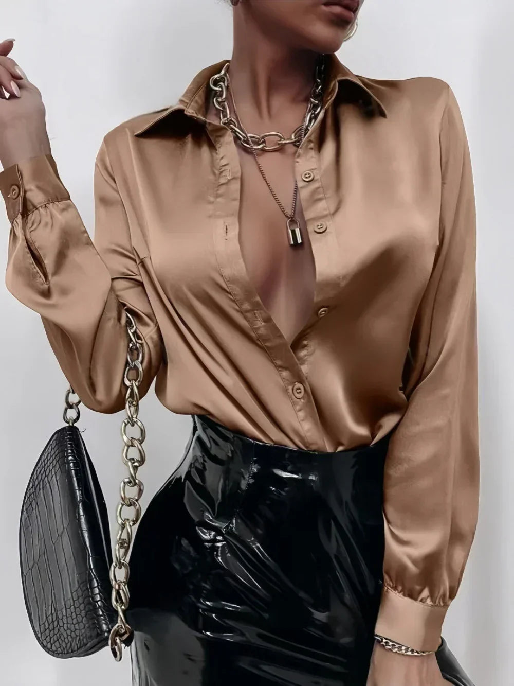 Woman wearing a satin bronze blouse and black vinyl high-waisted skirt, chain necklace, and croc-textured handbag