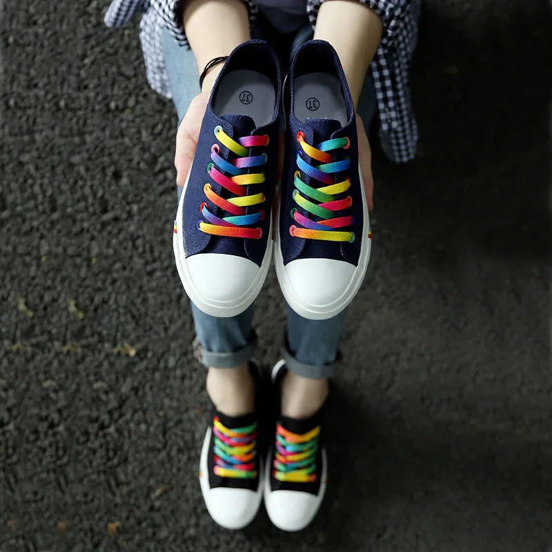 Navy canvas sneakers with white toe caps and rainbow laces, casual streetwear style.