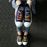 Navy canvas sneakers with white toe caps and rainbow laces, casual streetwear style.