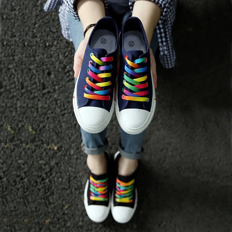 Navy canvas sneakers with white toe caps and rainbow laces, casual streetwear style.