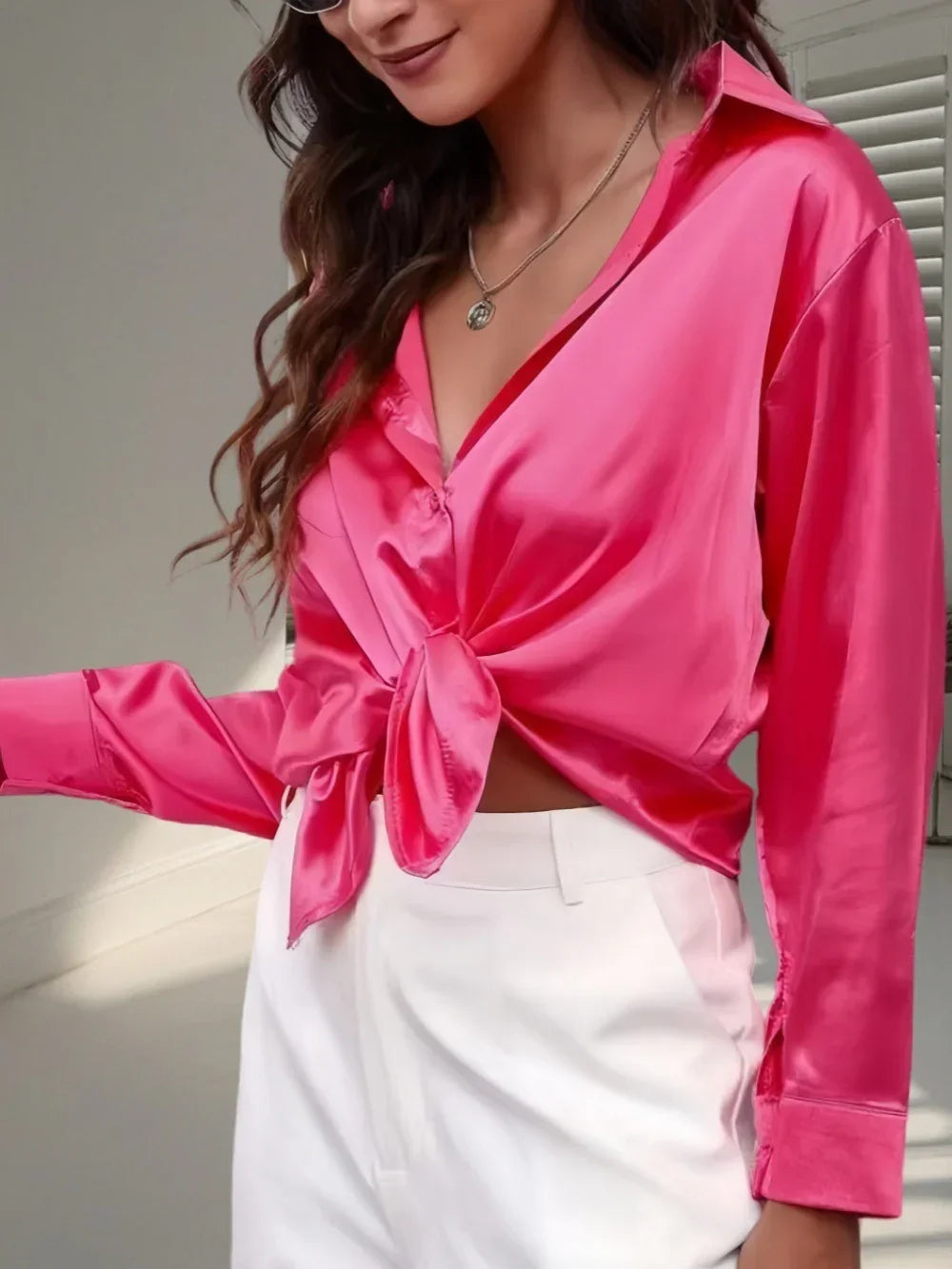 Woman wearing a pink satin long-sleeve blouse with front tie and white high-waisted pants