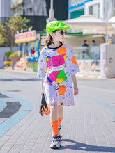 Girl wearing oversized white graphic t-shirt dress, neon green cap, orange socks, street style